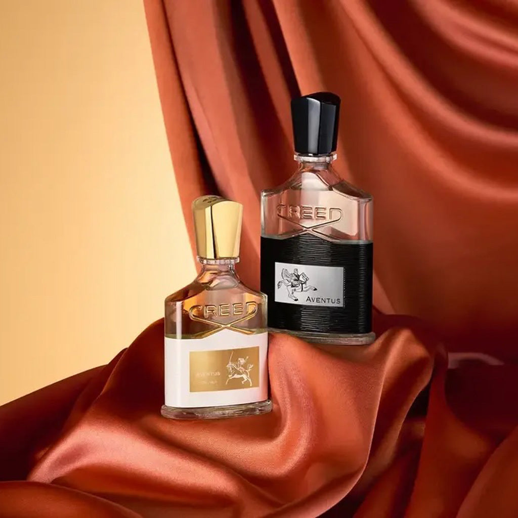 Two Creed perfume bottles on a draped fabric background